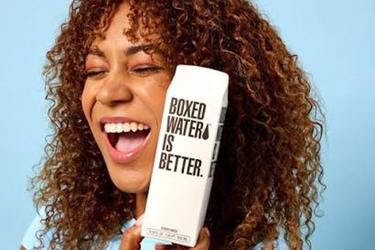 A smiling woman holding a Boxed Water carton