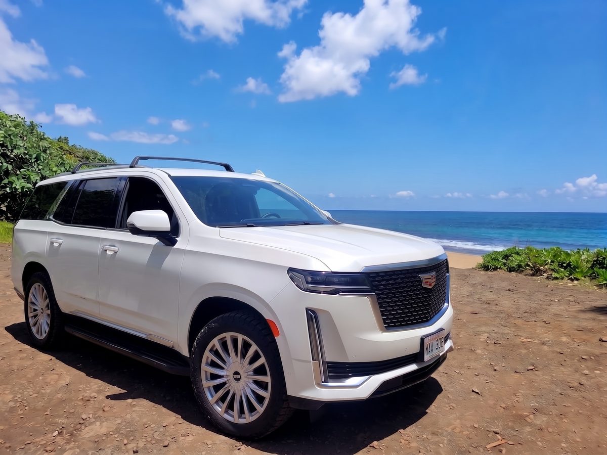 White Cadillac Escalade parked above a Maui beach with the ocean behind
